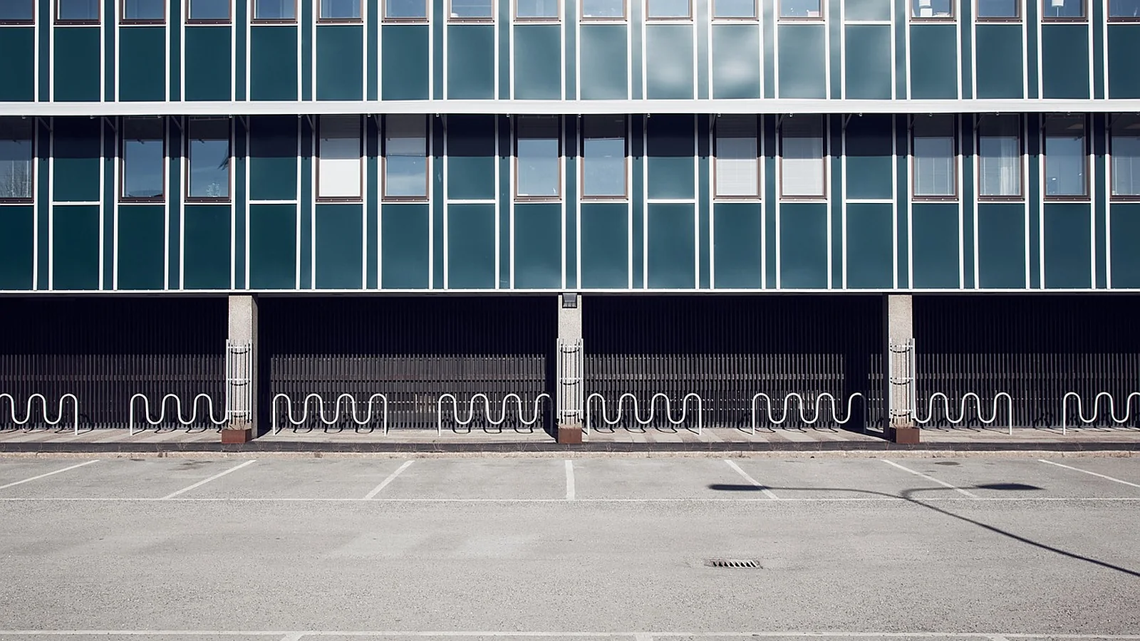 Mid-rise office building with rows of windows behind an empty asphalt parking lot under an overcast sky